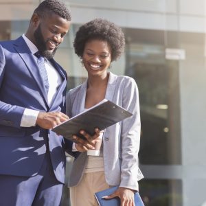 Happy couple of african american business partners working while standing outdoors, discussing new project. Blurred background with copy space